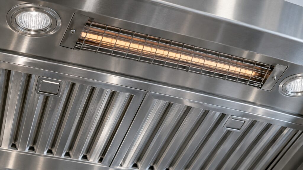 Close-up of the underside of a stainless range hood with its metal filters with the heating element visible, seen at eye level from the side, with nothing else in the frame.