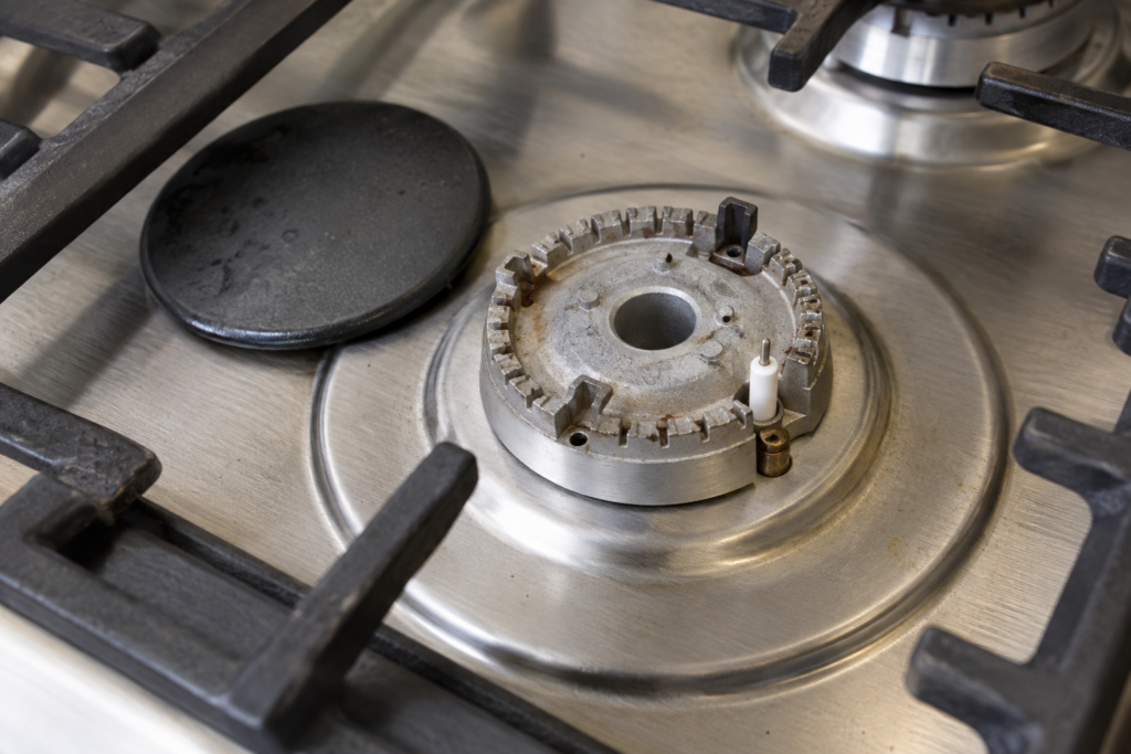 A gas cooktop burner with its cap removed, showing the spark igniter electrode beside the burner ring.