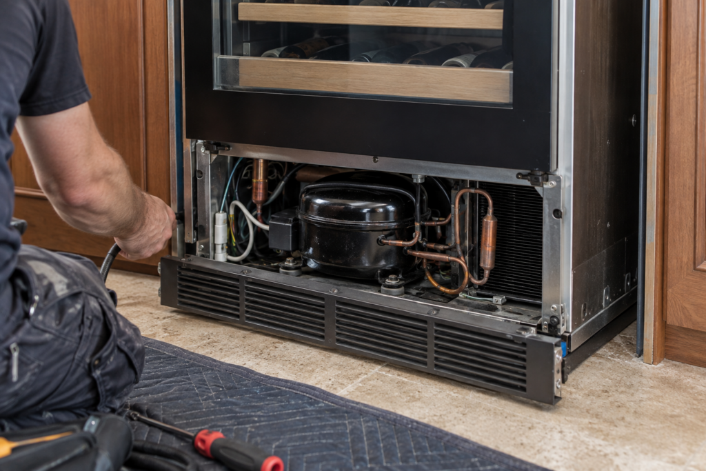 The compressor compartment at the base of a built-in wine refrigerator cabinet, pulled out from surrounding cabinetry.